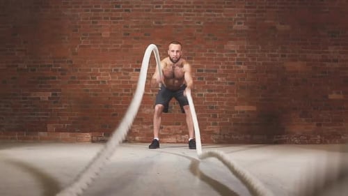 Athletischer junger Mann mit Kampfseil bei Übungen im Functional Training Fitness Gym