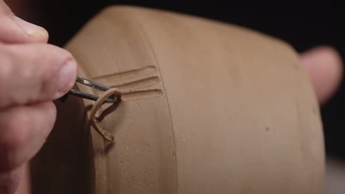 Potter's Hand schneidet Muster in Form von Stöcken auf glattem Tonprodukt mit Schaber aus
