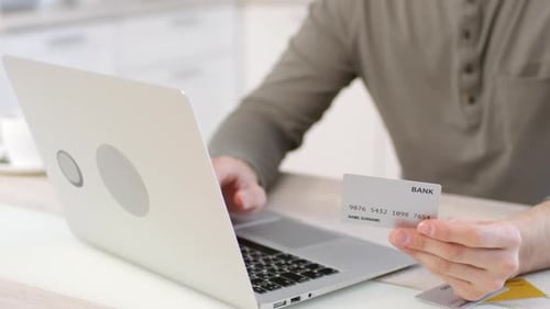 Man Types on Laptop Holding a Credit Card