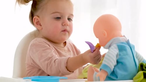 Adorable Child Pretends to Feed Doll at Table