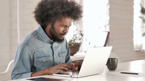 Frustrated Man Working on Laptop in Modern Workspace