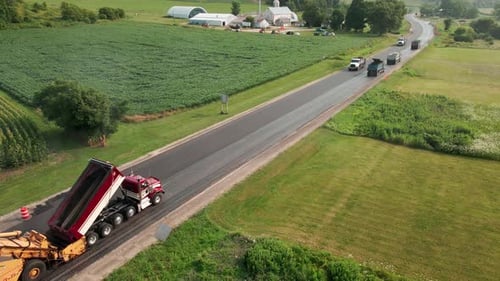 Straßenpersonal arbeitet an der Instandsetzung eines Abschnitts der Landstraße. Mehrere Muldenkipper liefern Asphalt.