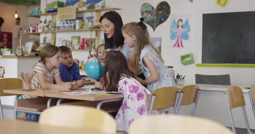 Female Teacher with Kids in Geography Class Looking at Globe