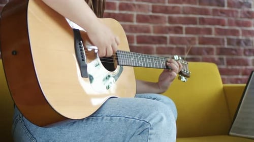 Young Adult Plays Guitar on Sofa at Home