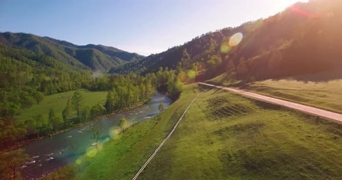 Mid Air Flight Over Fresh Mountain River and Meadow at Sunny Summer Morning, Rural Dirt Road Below