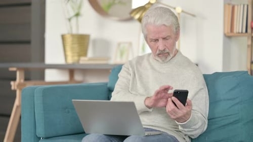 Senior Man Using Smartphone and Laptop at Home