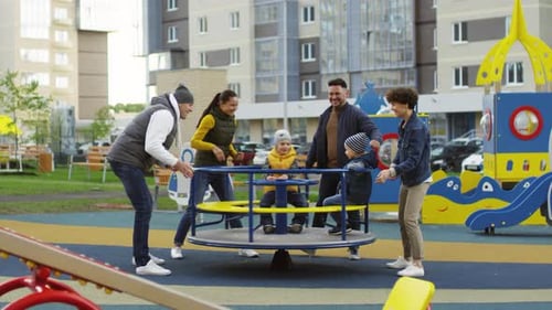 Two Couples Spinning Roundabout for Young Sons on Playground