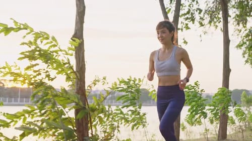 Asian young beautiful woman running for health in the evening sunset on street in public park.