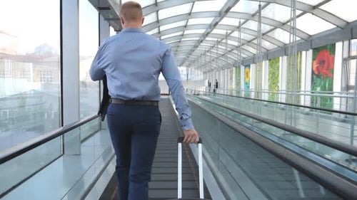 Unrecognizable Businessman Running on Escalator in Hall of Terminal and Pulling Suitcase on Wheels