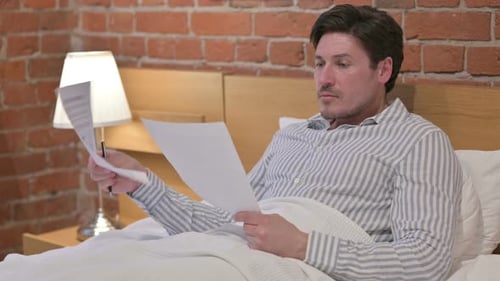 Man Reading Documents in Bed at Home