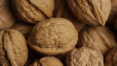 Cinematic, rotating shot of walnuts in their shells on a white surface