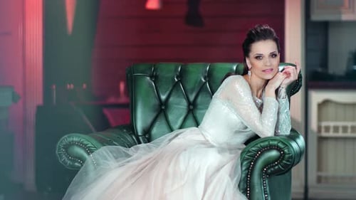 Mujer de lujo sonriente posando con un increíble vestido blanco glamuroso sentada en un sillón mirando a la cámara