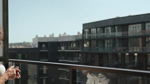 Woman Relaxing on Balcony Overlooking Cityscape on Sunny Day