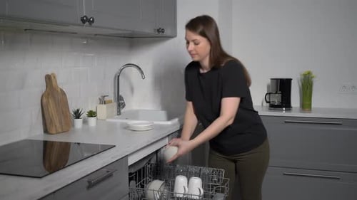 Woman Loading Dishes Into Modern Kitchen Dishwasher