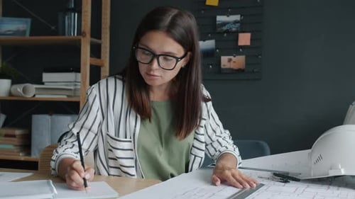 Serious Female Architect Measuring Construction Plan with Tools and Writing Working in Office