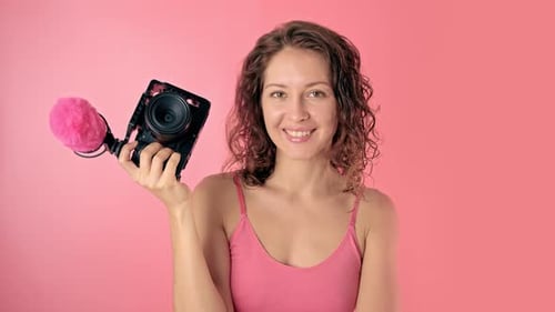 Woman Smiling Holding Camera in Front of Pink Backdrop