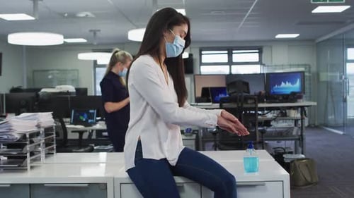 Woman wearing face mask sanitizing her hands at office