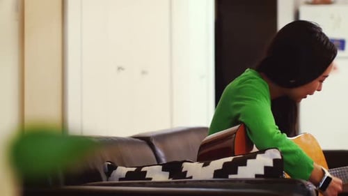 Woman Playing Guitar on Couch at Home