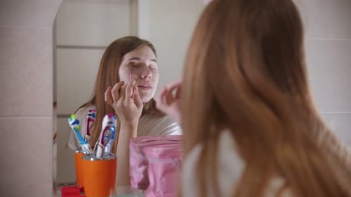Woman Applies Makeup in Brightly Lit Bathroom Mirror