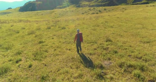 Flight Over Backpack Hiking Tourist Walking Across Green Mountain Field. Huge Rural Valley at Summer