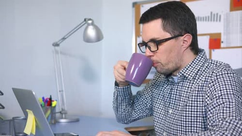 Männlicher Computerbenutzer, der auf der Tastatur tippt, auf den Bildschirm schaut und Kaffee trinkt