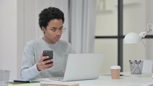 Woman Uses Smartphone While Working at Laptop