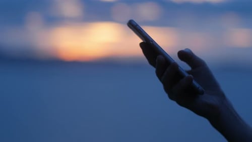 Hand Holding Smartphone at Sunrise or Sunset