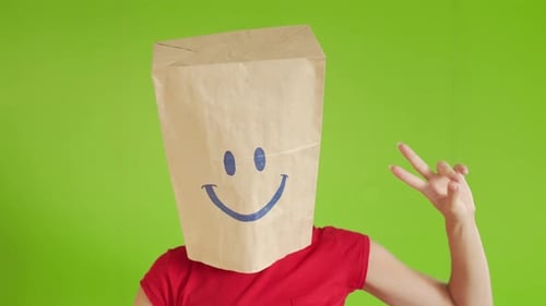 Eine verrückte Frau gestikuliert mit einer Pappschachtel auf dem Kopf mit einem Smiley-Gesicht auf einem Greenscreen