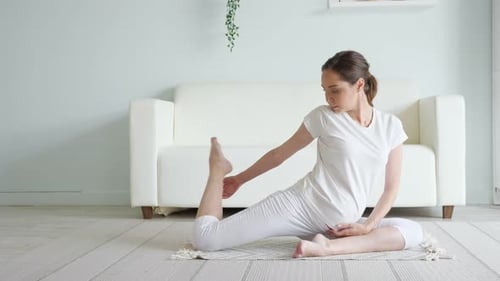Une femme enceinte calme fait la pose d'Ardha Matsyendrasana à la maison