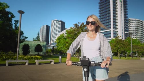 Young beautiful girl rides electric scooter in summer along street,