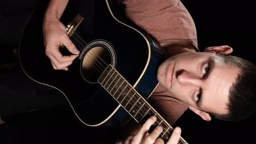 Vertikales Video. Young Man Blogger spielt eine Akustikgitarre auf schwarzem Hintergrund