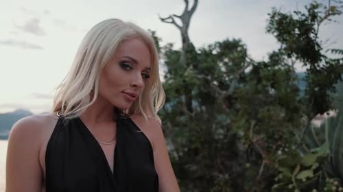 Beautiful blonde woman in black dress walking at sunset against the sea