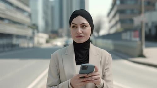 Geschäftsfrau im Hijab benutzt Handy beim Gehen