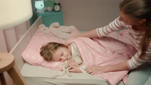 Mother Tucking Child in Bed at Night