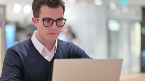 Young Adult Works Thoughtfully on Laptop at Desk
