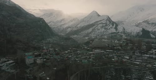 Breite rotierende Aufnahme von Häusern, die sich über dem Berg mit schneebedeckten Bergen im Hintergrund aufbauen.