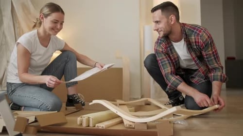 Young Adults Moving in New Home. Couple Moving in Assembling Chair Furniture. Young Interracial