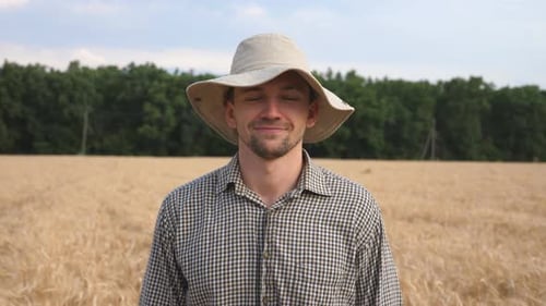 Close Up of Happy Smiling Farmer in Hat Looking Into Camera Against the Blurred Background of Wheat
