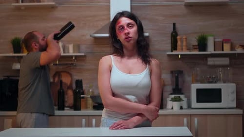 Distressed Woman with Bruised Eye Stands in Kitchen