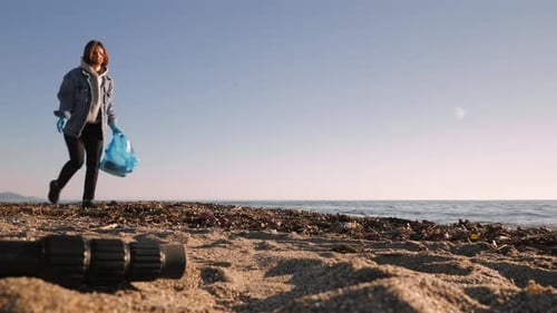 Voluntaria mujer recogiendo basura plástica en una bolsa en una playa contaminada.