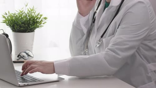 Female Woman Doctor in Hospital Office Room Cabinet Working Laptop Talking Phone