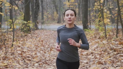 Sportswoman in black and grey sportswear running in the park. Motivated woman running in the forest