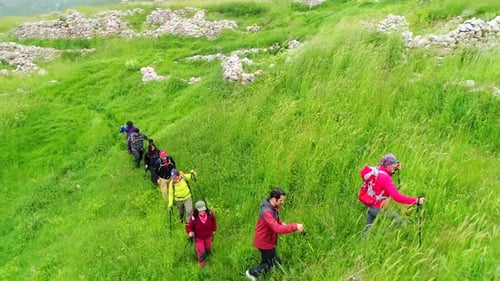Hikers Walk Across Grassy Green Mountainside