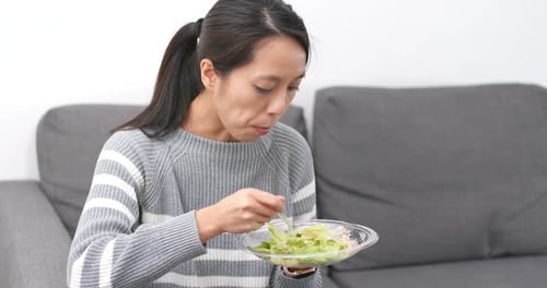 Young Woman Eating Salad on Sofa Indoors