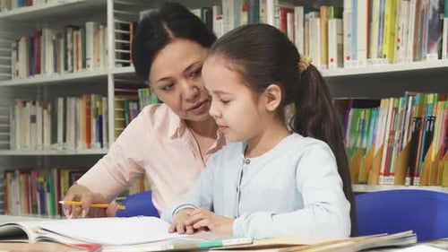 Woman Helping Young Girl With Homework in Library