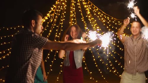 Friends Celebrate with Sparklers Under Fairy Lights