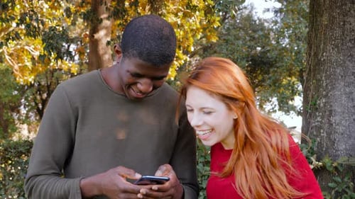 portrait of happy young interracial couple using smartphone in the park smiling