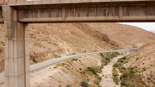aerial slow backward drone shot under empty train bridge, revealing the mountains, an empty side roa