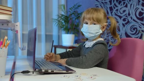 Child Wearing Mask Draws on Laptop at Desk
