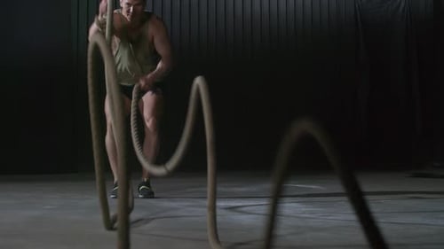 Muscular Man Exercising With Battle Ropes in Dark Gym